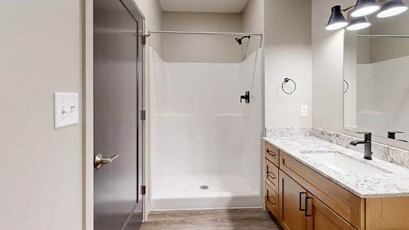 Modern apartment bathroom with a tub and shower, single-sink vanity, and wood cabinetry.