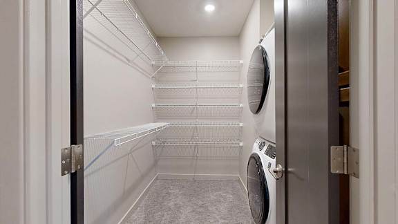 Apartment laundry closet with a stacked washer and dryer and built-in wire shelving.