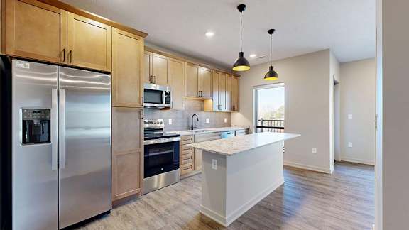 Modern apartment kitchen with a large island, wood cabinetry, and stainless steel appliances.