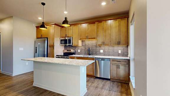 Modern apartment kitchen with a large island, wood cabinetry, and stainless steel appliances.