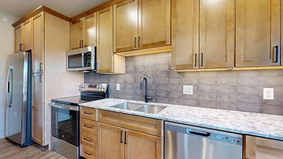 Modern apartment kitchen with wood cabinetry, stainless steel appliances, and a tile backsplash.