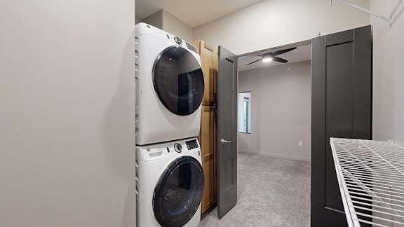 Apartment laundry closet with a stacked washer and dryer and wire shelving.