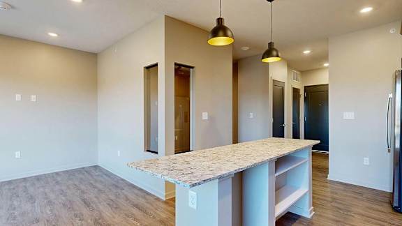 Open apartment kitchen with a large island, pendant lighting, and wood-style flooring.