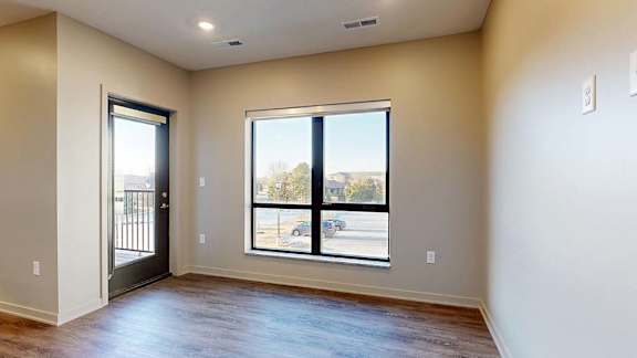 Bright apartment living area with wood-style flooring, large windows, and a door leading to a private balcony.