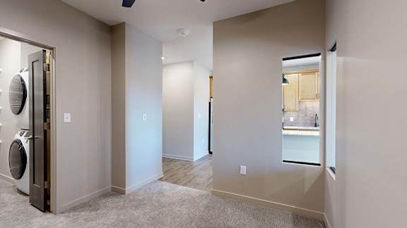 Apartment bedroom with carpeted flooring, a large window, and a laundry closet with a stacked washer and dryer.
