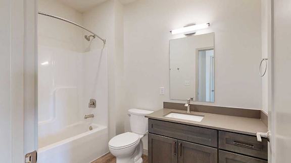 A bathroom with a quartz vanity, dark wooden cabinets, and a tub shower with brushed nickel fixtures.