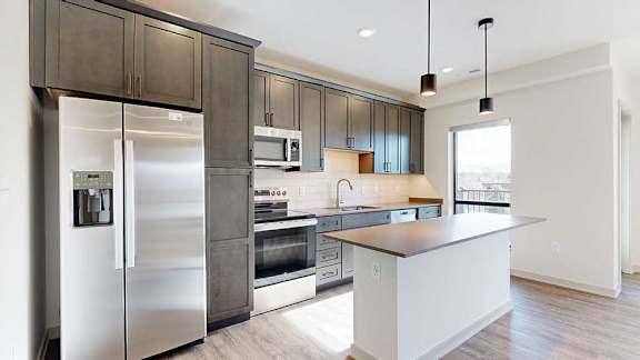 A kitchen with dark wooden cabinets, quartz countertops, a tile backsplash, an island, and a window over the kitchen sink.