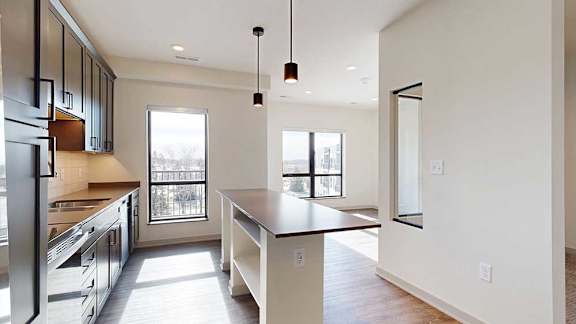 A kitchen with dark wooden cabinets, quartz countertops, a tile backsplash, an island, and a window over the kitchen sink.