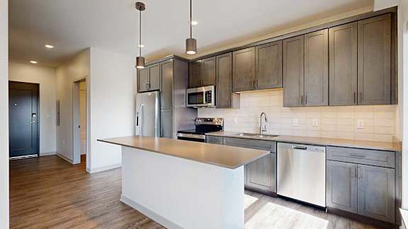 A kitchen with dark wooden cabinets, quartz countertops, an island, and stainless steel appliances.
