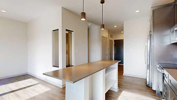 A kitchen with dark wooden cabinets and an island, in front of a sleeping area and living room.