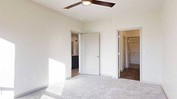 a bedroom with carpeted flooring, a ceiling fan, and an attached bathroom with walk-in closet
