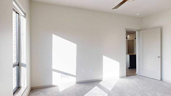 a bedroom with white walls, carpeted flooring, a ceiling fan, and a door to the living room