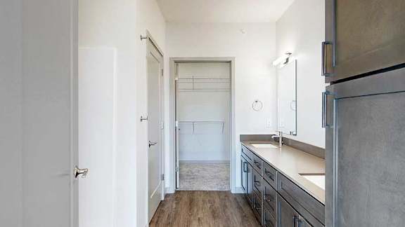a bathroom with a double vanity sink, two mirrors, a tall storage cabinet, and a walk-in closet at the end