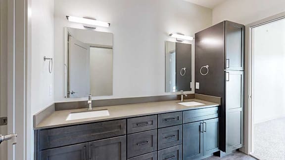 a bathroom with a double vanity sink, two mirror, and a tall storage cabinet