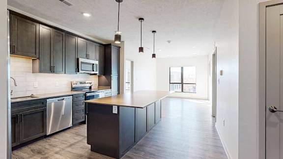a modern kitchen with a large central island, dark wood cabinets, and stainless steel appliances