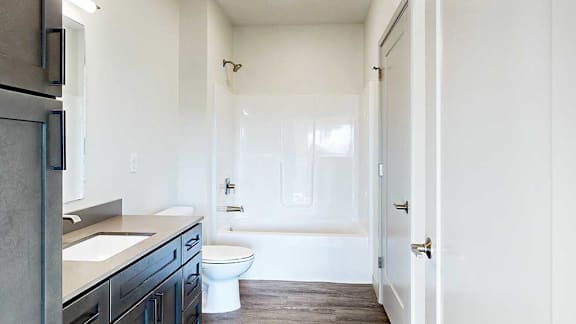 a bathroom with a quartz vanity sink, a shower tub, and doors to both the hallway and the second bedroom