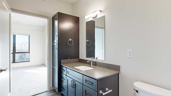 a bathroom with a quartz vanity sink, mirror, and a tall storage cabinet