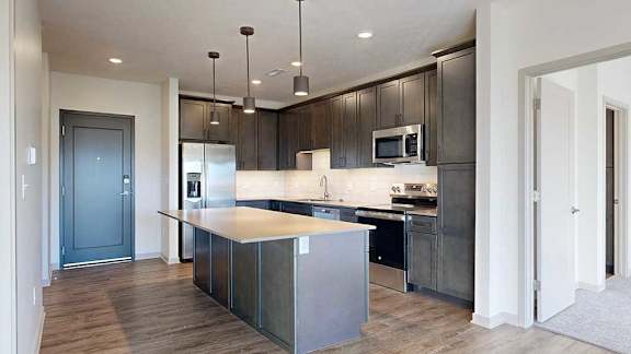 a modern kitchen with dark wood cabinets, an island, stainless steel appliances, quartz countertops, and a tile backsplash