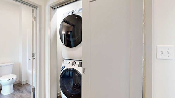a stackable full-sized washer and dryer in a laundry closet in the hallway