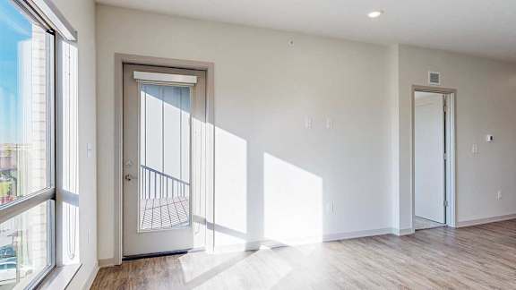 a living room with a door to the balcony, a window, and a door to a bedroom