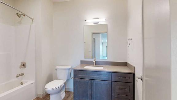A bathroom with a quartz vanity, dark wooden cabinets, and a tub shower with brushed nickel fixtures.