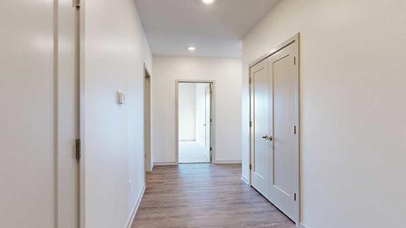 A hallway with a closet to the side, and an open door to a bedroom at the end.