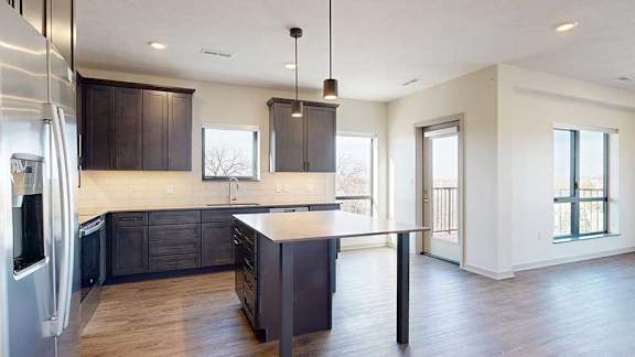 A kitchen with dark wooden cabinets and a large island, open to a living room with floor-to-ceiling windows.