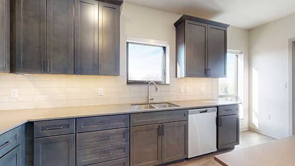 A kitchen with dark wooden cabinets, quartz countertops, a tile backsplash, and a window over the kitchen sink.