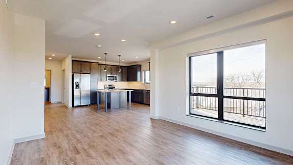A living room with floor-to-ceiling windows open to a kitchen with a large island with dark cabinets.