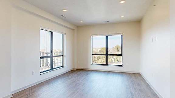 A living room with hardwood-style flooring and floor-to-ceiling windows.