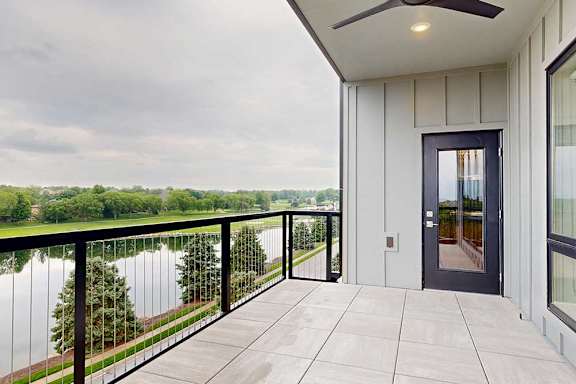 A balcony with a windowed-door to the kitchen, tiled flooring, a metal railing, a ceiling fan, and a stunning view of the neighboring golf course.