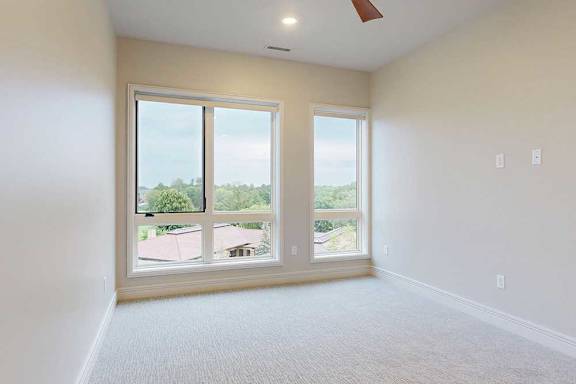 A carpeted bedroom with floor-to-ceiling windows and a ceiling fan.