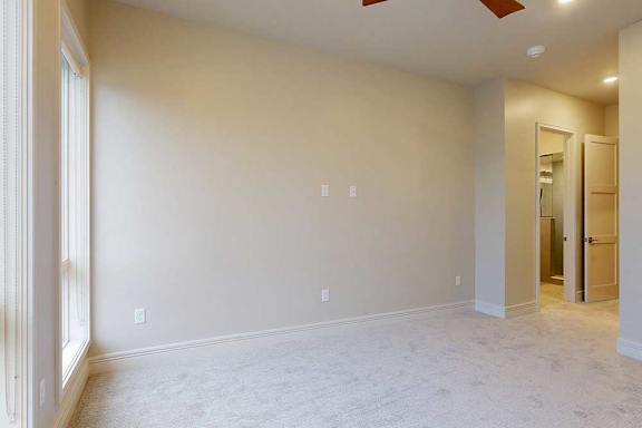 A carpeted bedroom with floor-to-ceiling windows, a ceiling fan, and an ensuite bathroom.