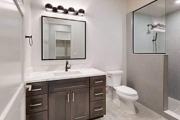A bathroom with a wide quartz vanity sink, a modern framed mirror with overhead lighting, and a tiled walk-in shower with a half wall and glass window.