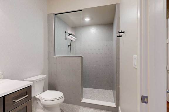 A tiled walk-in shower with a half wall, glass window, and a shower head with detached sprayer.
