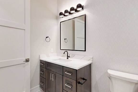 A bathroom with a dark wood and light quartz vanity sink, with a framed mirror and overhead lighting.