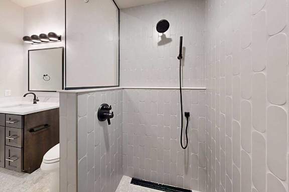 A tiled walk-in shower with a half wall, glass window, and a shower head with detached sprayer.