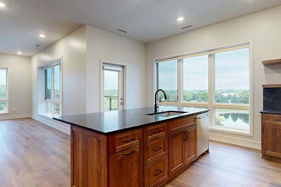 A gourmet kitchen island with quartz countertops, overlooking a living room and dining area with floor-to-ceiling windows.