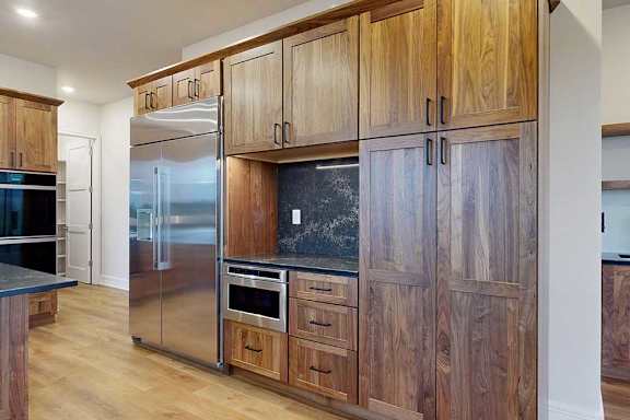 A gourmet kitchen with an oversized stainless steel fridge, two stainless steel ovens, and oak wooden cabinets.