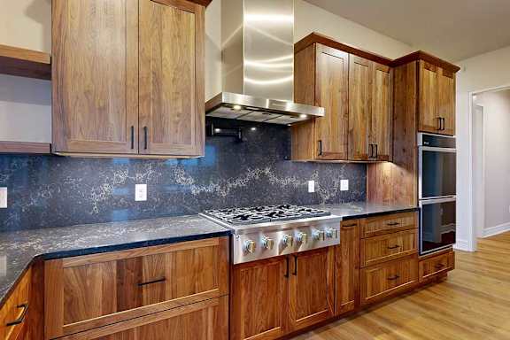 A gourmet kitchen with a stainless steel range hood over a 6-burner gas stovetop, a pot filler faucet, two stainless steel ovens, and oak cabinets.