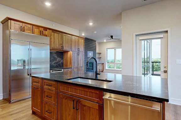 A gourmet kitchen with an oversized island, oak wooden cabinetry, stainless steel appliances, quartz countertops, a range hood, and a tile backsplash.
