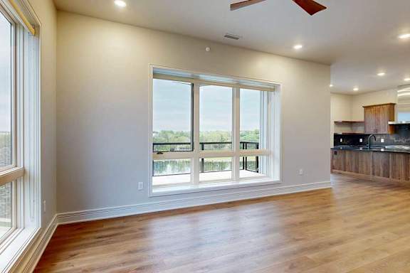 A spacious living room with floor-to-ceiling windows and hardwood flooring, open to a gourmet kitchen.