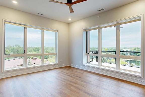 A living room with floor-to-ceiling windows, hardwood flooring, and a ceiling fan.