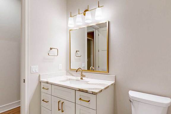A hallway bathroom with a white vanity sink with golden accents and fixtures.