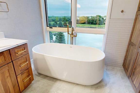 A spacious ensuite bathroom with a double vanity sink, floor-to-ceiling window, soaking tub, and tiled flooring.