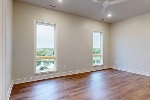 A bedroom with floor-to-ceiling windows, hardwood flooring, and a ceiling fan.