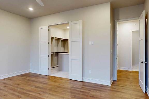 A bedroom with a walk-in boutique-style closet, and hardwood flooring.