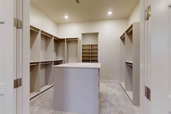 A spacious boutique-style walk-in closet with built-in shelves, and a central cabinet.