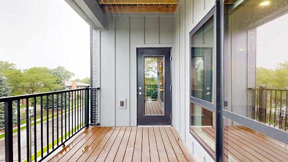 A balcony with a metal railing, a windowed door to the living room, and a view of the neighborhood.