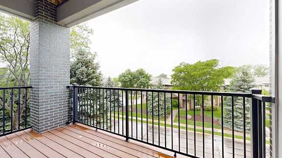 A balcony with a metal railing, a brick pillar, and a view of the neighborhood.